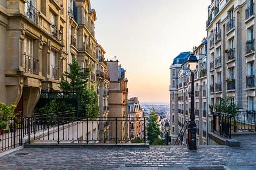 Una strada acciottolata in collina, fiancheggiata da palazzi, con vista sullo skyline della città al tramonto.