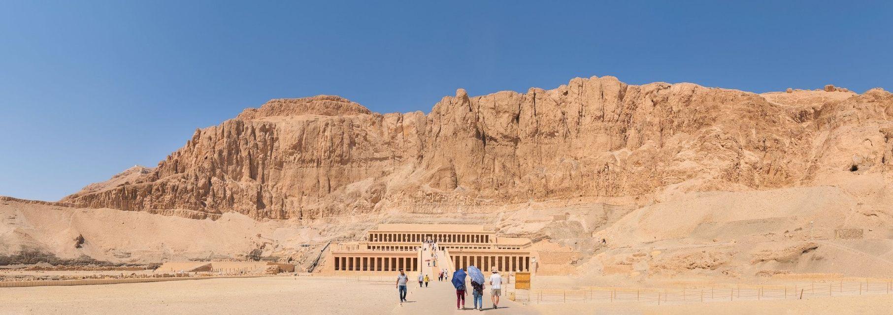Eine WeRoad-Gruppe wandert auf einen großen, terrassierten antiken Tempel zu, der in den Fuß einer Felswand in der Wüste gebaut ist.