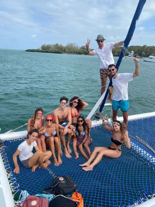 Un viaggio di gruppo WeRoad con persone che posano e sorridono insieme sulla rete blu di un catamarano in mare.