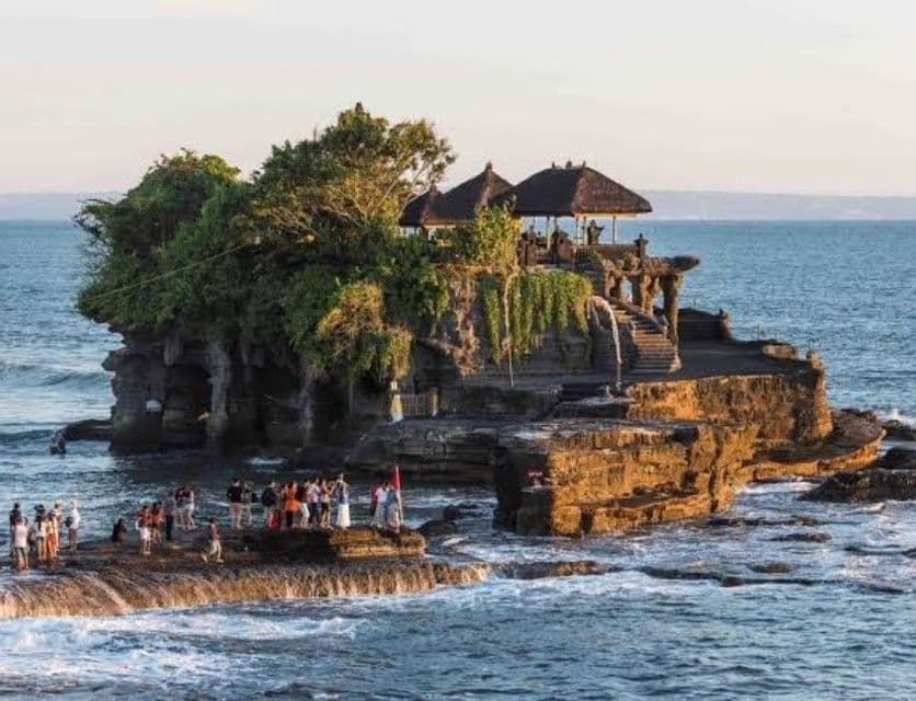 Un viaje en grupo de WeRoad se encuentra sobre las rocas frente a un templo tradicional construido en una pequeña y exuberante isla en el océano.