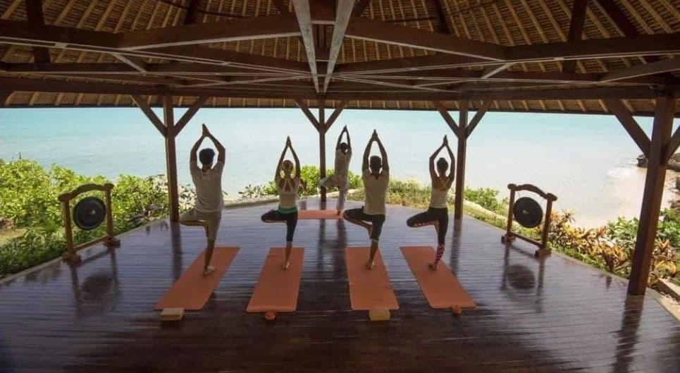 Un viaje en grupo de WeRoad practicando yoga en la postura del árbol en un pabellón al aire libre con vistas al océano.