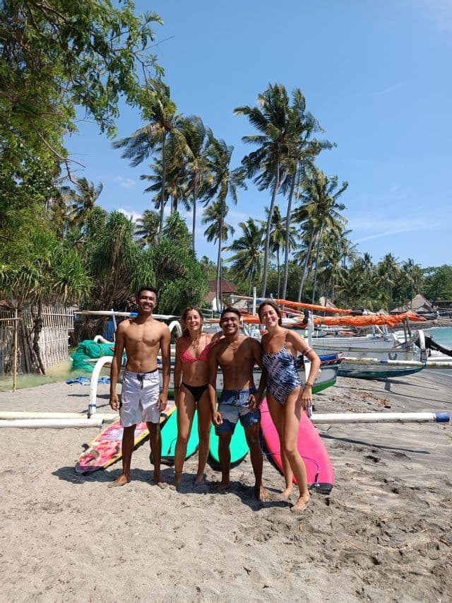 Un viaje en grupo de WeRoad de cuatro personas en traje de baño posando con sus tablas de surf en una playa de arena con palmeras.
