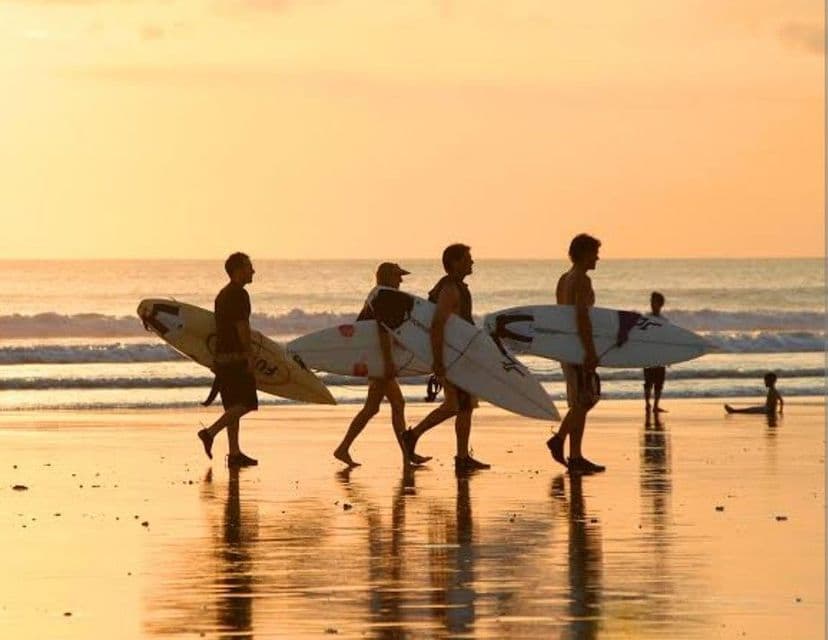 Un viaje en grupo de WeRoad con cuatro surfistas en silueta, llevando sus tablas y caminando por la orilla al atardecer.
