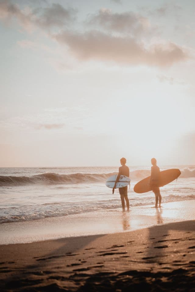 Dos surfistas con sus tablas de surf de pie en el agua poco profunda del océano al atardecer.