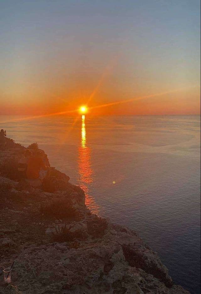Un viaggio di gruppo WeRoad su una scogliera rocciosa, ammirando il tramonto sull'oceano calmo.