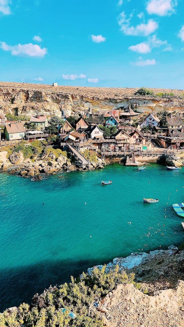 Ein farbenfrohes Dorf, das in eine felsige Klippe gebaut wurde und eine kleine Bucht mit türkisfarbenem Wasser und mehreren Booten überblickt.