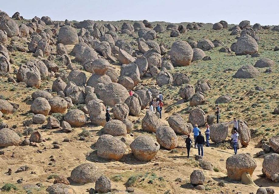 Un voyage en groupe WeRoad arpente un chemin à travers un paysage vallonné parsemé de grandes formations rocheuses sphériques sous un ciel clair.