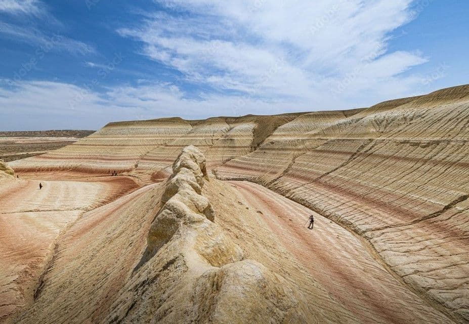 Un viaje en grupo de WeRoad haciendo senderismo por un vasto paisaje de colinas coloridas y a rayas bajo un cielo parcialmente nublado.