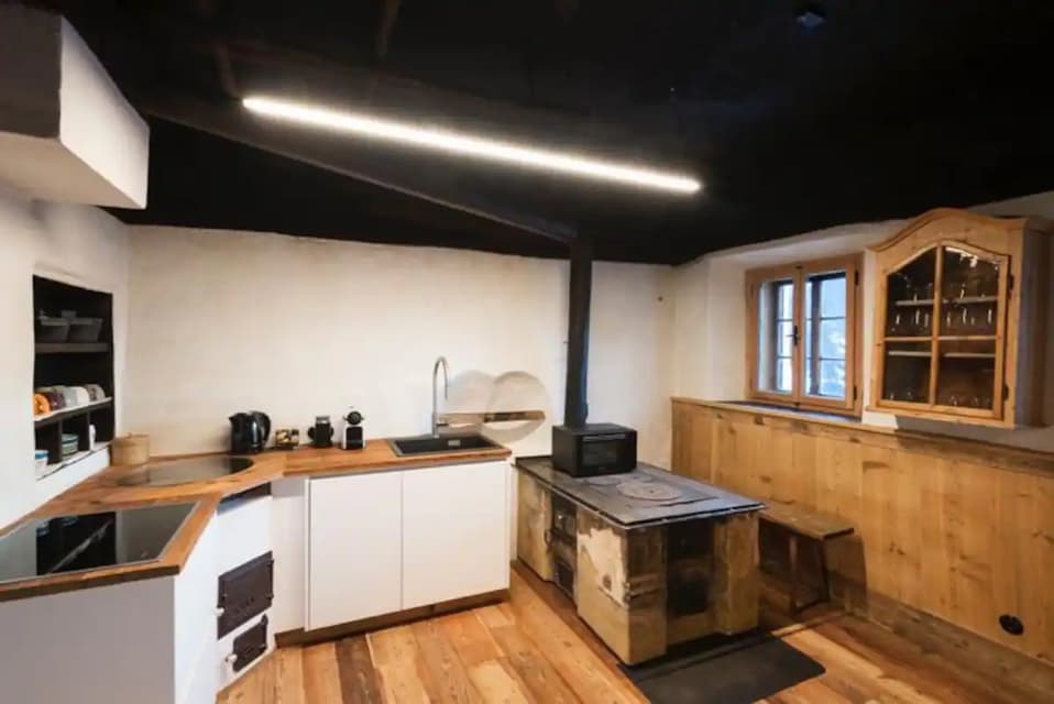 Una cucina rustica con moderni armadietti bianchi, ripiani e pavimenti in legno, e una tradizionale stufa a legna.