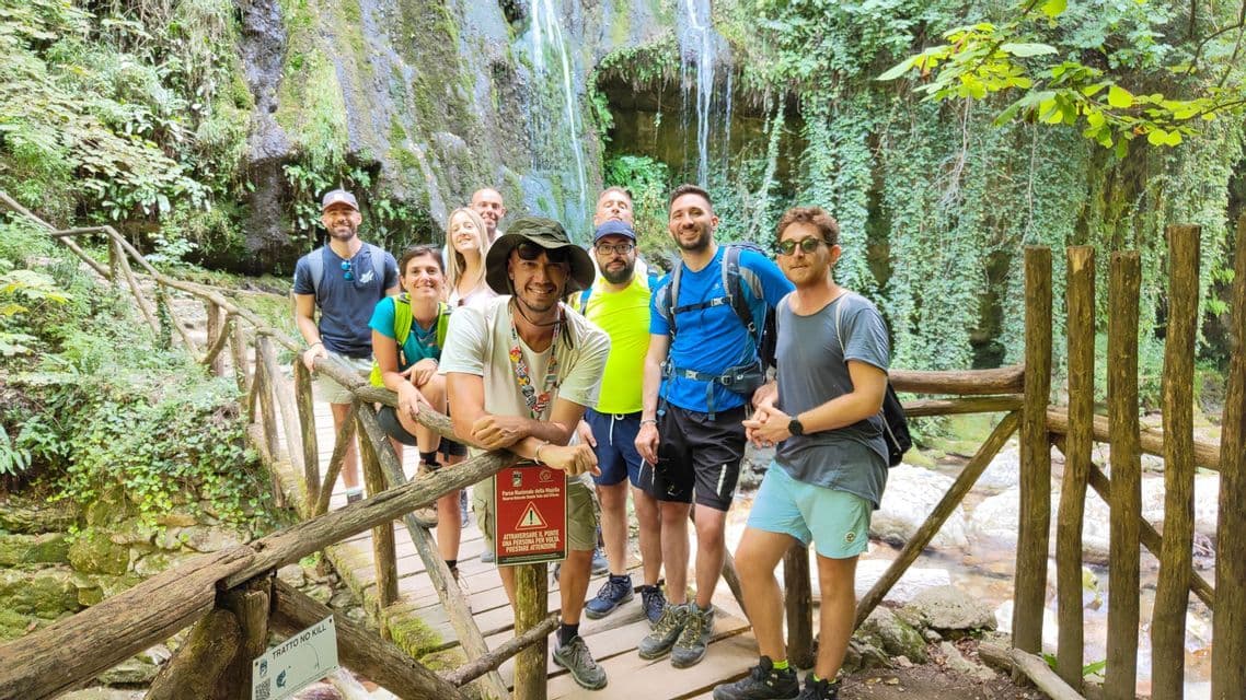 Un gruppo WeRoad in posa per una foto su un ponte di legno in una foresta rigogliosa con una cascata sullo sfondo.
