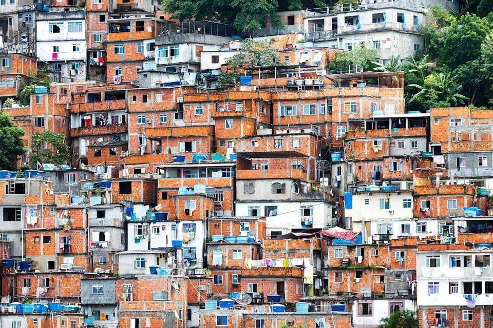 Fitte costruzioni in mattoni rossi e bianchi di una favela che ricoprono una collina verde.