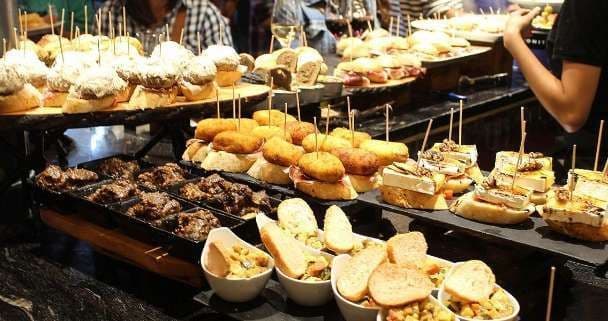 Un'ampia varietà di pintxos e tapas spagnoli disposti su un bancone da bar scuro in un ristorante.