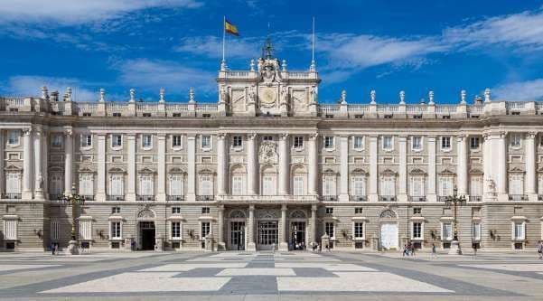 La grandiosa facciata di un palazzo storico si erge dietro una grande piazza pavimentata sotto un cielo azzurro limpido