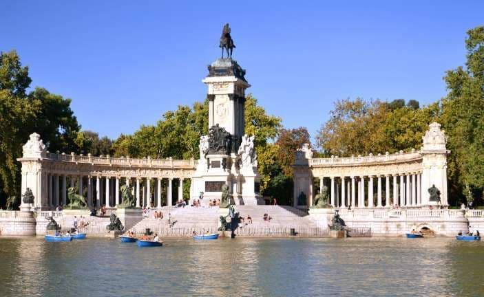 Un grande monumento con una statua equestre in cima si erge sulla riva di un lago con persone in barche a remi.