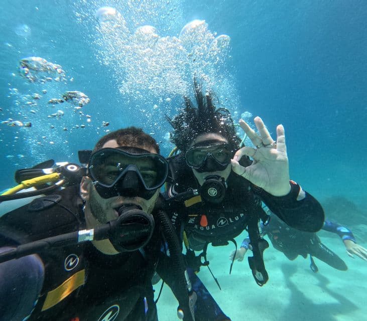 Due persone in un viaggio di gruppo WeRoad si scattano un selfie subacqueo durante un'immersione, con uno che fa il segno OK con la mano.