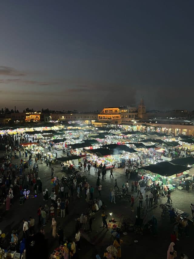 Una vista sopraelevata di un vivace mercato all'aperto di notte, con folle di persone che camminano tra bancarelle illuminate a festa.