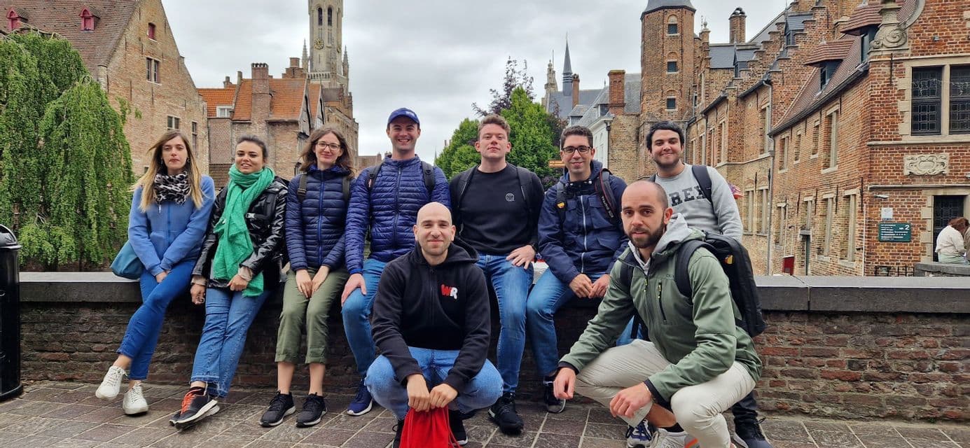 Un viaje en grupo de WeRoad de nueve personas posando juntas en un muro de ladrillo en un pueblo histórico europeo bajo un cielo nublado.