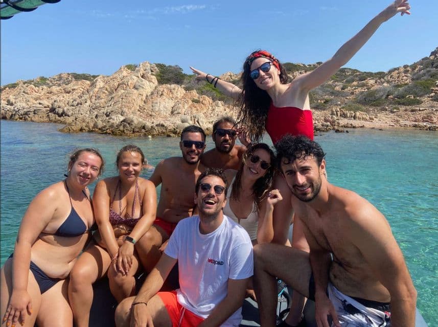 Un grupo de WeRoad sonríe para una foto en un barco en aguas cristalinas de color turquesa, cerca de acantilados rocosos.