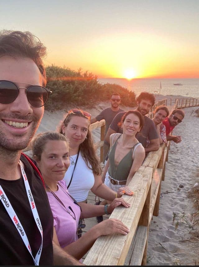 Un viaje en grupo de WeRoad se toma una selfie en un malecón de madera en una playa de arena al atardecer.