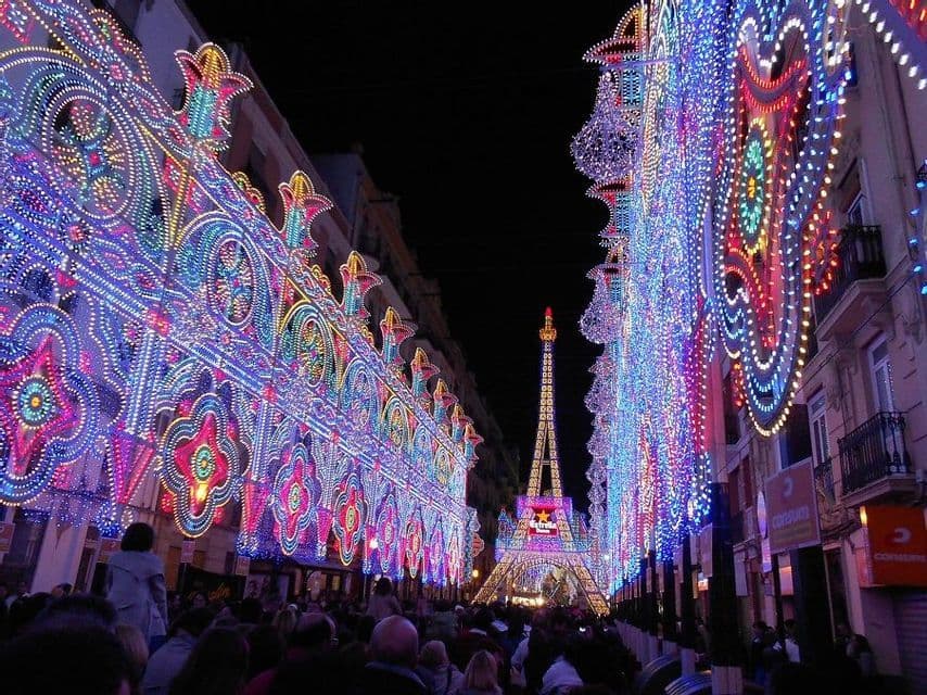 Elaborate installazioni luminose multicolori illuminano un affollato festival di strada di notte, con una replica della Torre Eiffel sullo sfondo.