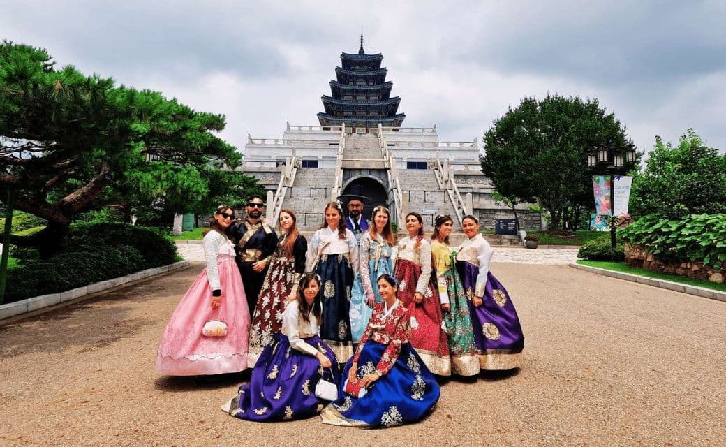 Un viaggio di gruppo WeRoad in posa con colorati abiti tradizionali hanbok davanti a una grande pagoda sotto un cielo nuvoloso.