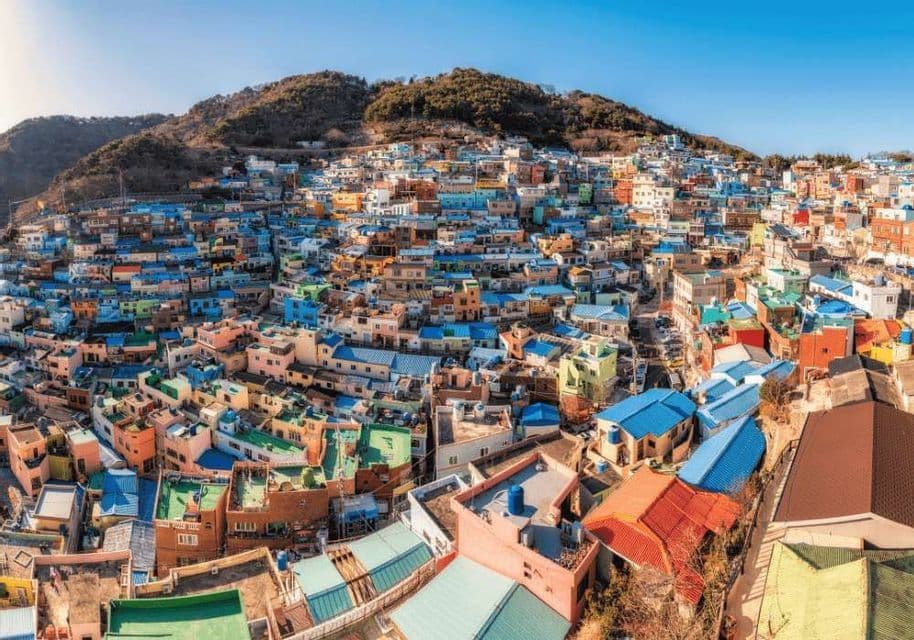 Un fitto villaggio di case colorate con tetti blu, arroccato su un verde fianco di montagna sotto un cielo azzurro e limpido.