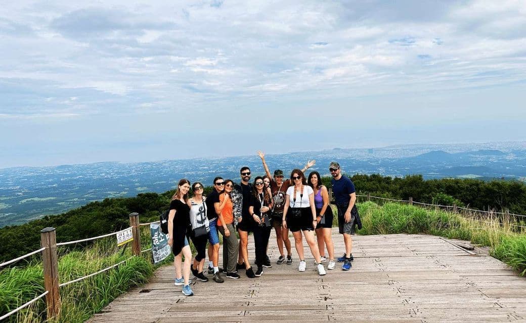 Un gruppo WeRoad in viaggio posa per una foto su un belvedere di legno che si affaccia su un vasto paesaggio di colline e una città lontana.