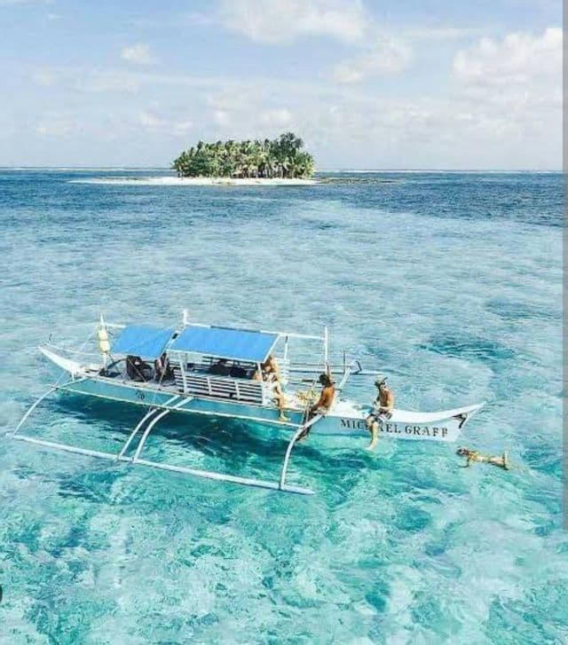 Un viaje en grupo de WeRoad en una canoa polinesia flotando en aguas turquesas cristalinas, con una pequeña isla tropical a lo lejos.