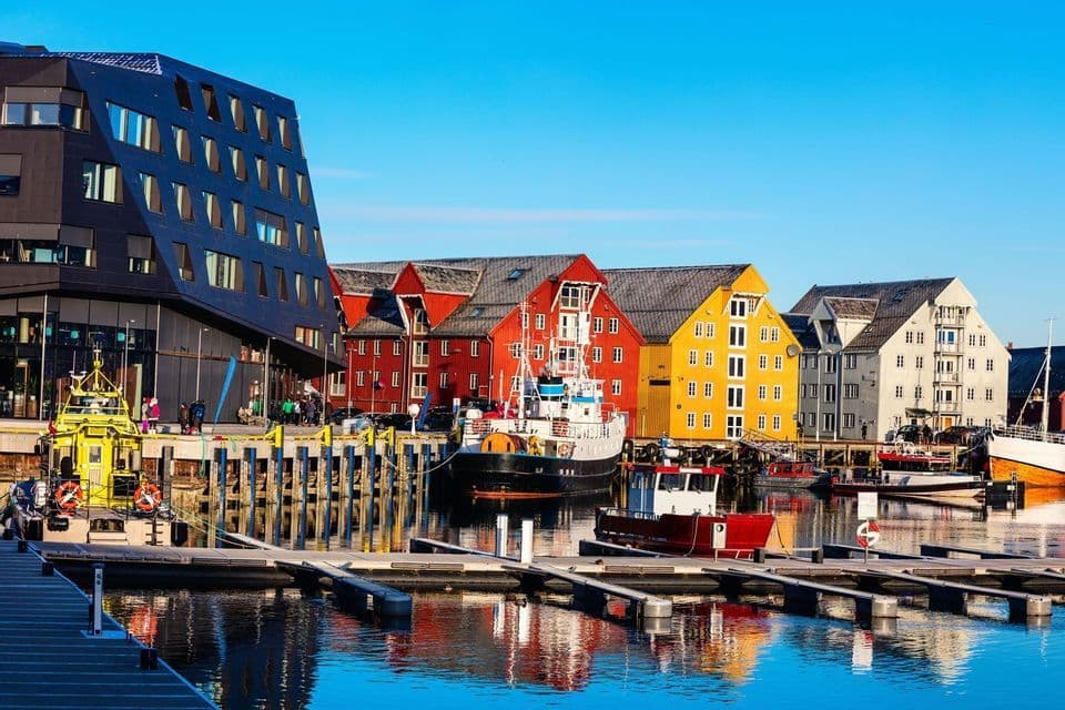 Ein Hafen mit festgemachten Booten, gesäumt von farbenfrohen traditionellen Häusern und einem modernen Gebäude, unter strahlend blauem Himmel.
