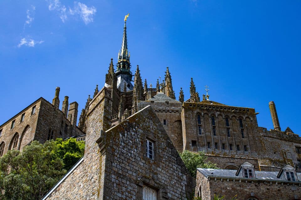 Vue en contre-plongée d'une abbaye gothique historique avec une haute flèche centrale s'élançant vers un ciel bleu éclatant.