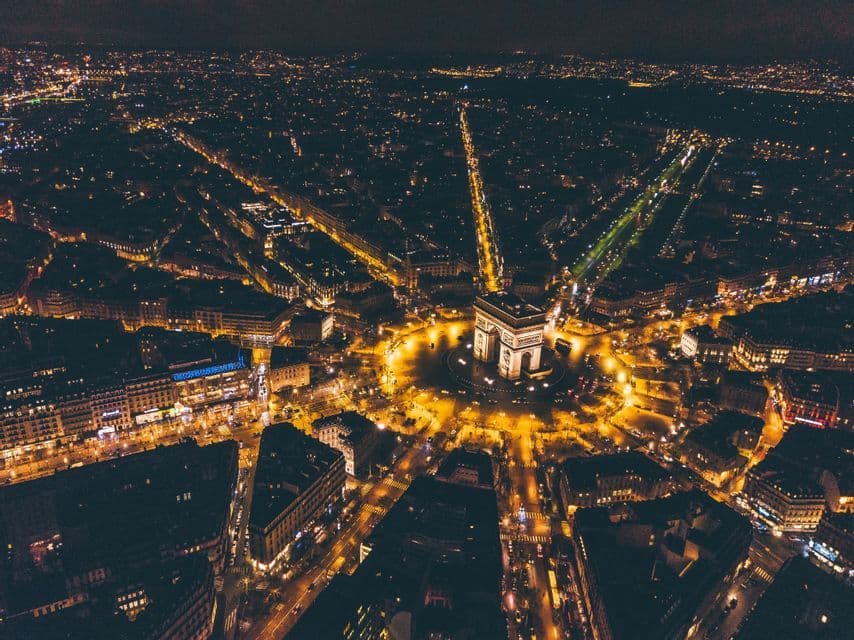 Vue aérienne d'un arc monumental illuminé au centre d'un rond-point, avec les rues de la ville rayonnant la nuit.