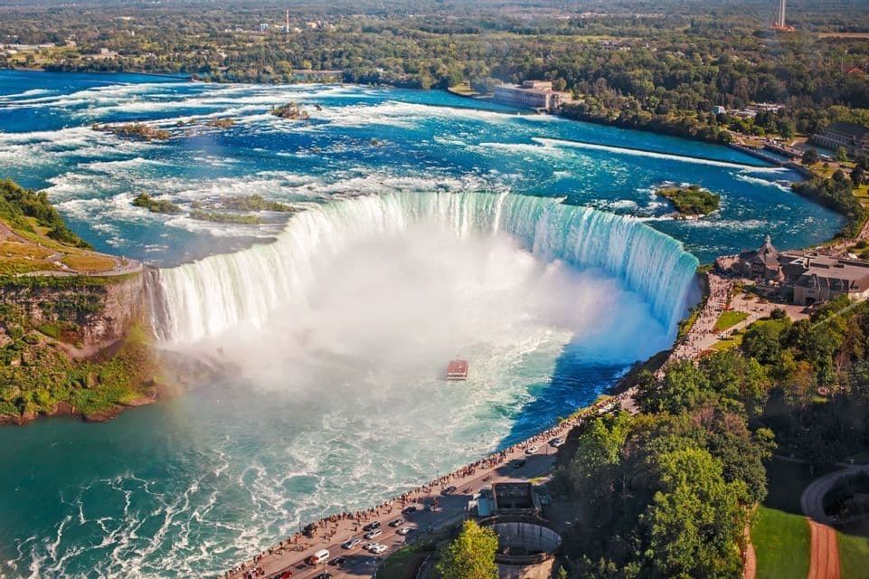 Vista aérea de una gran cascada en forma de herradura, con un barco navegando las aguas brumosas y turistas en la orilla.