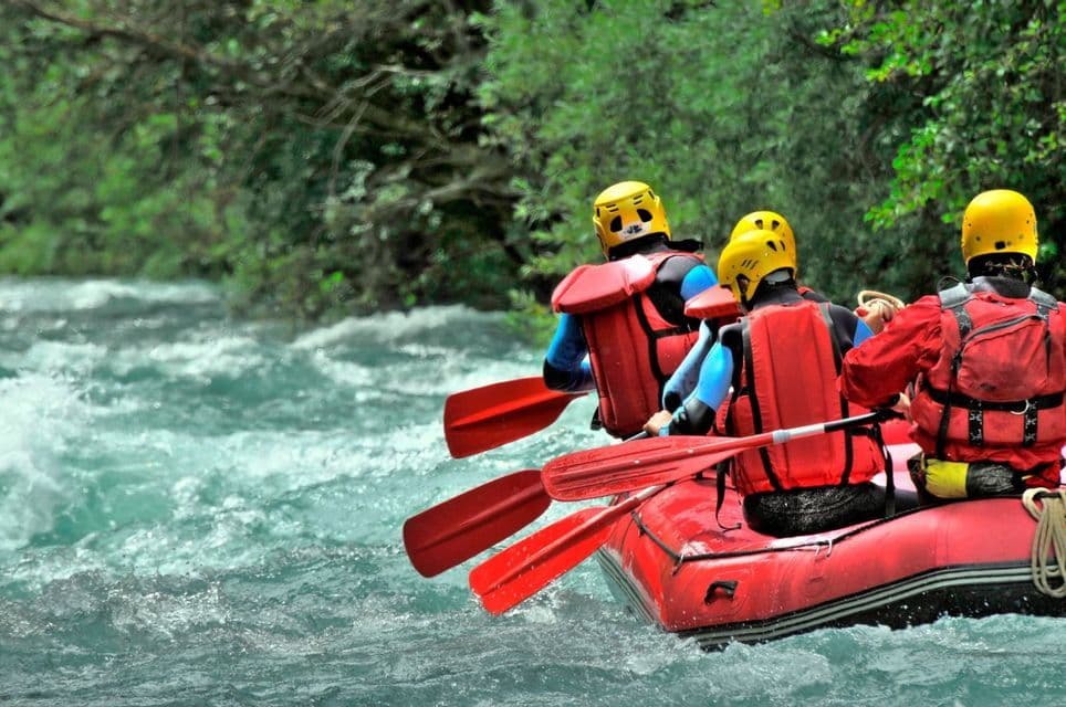 Un grupo de WeRoad haciendo rafting en un bote inflable rojo en un río de aguas bravas, visto desde atrás mientras reman.