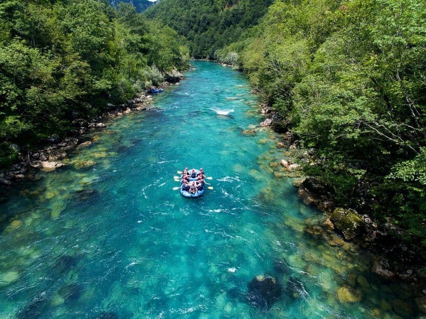 Vista aerea di un viaggio di gruppo WeRoad che fa rafting in gommone su un vibrante fiume turchese, circondato da foreste verdi.