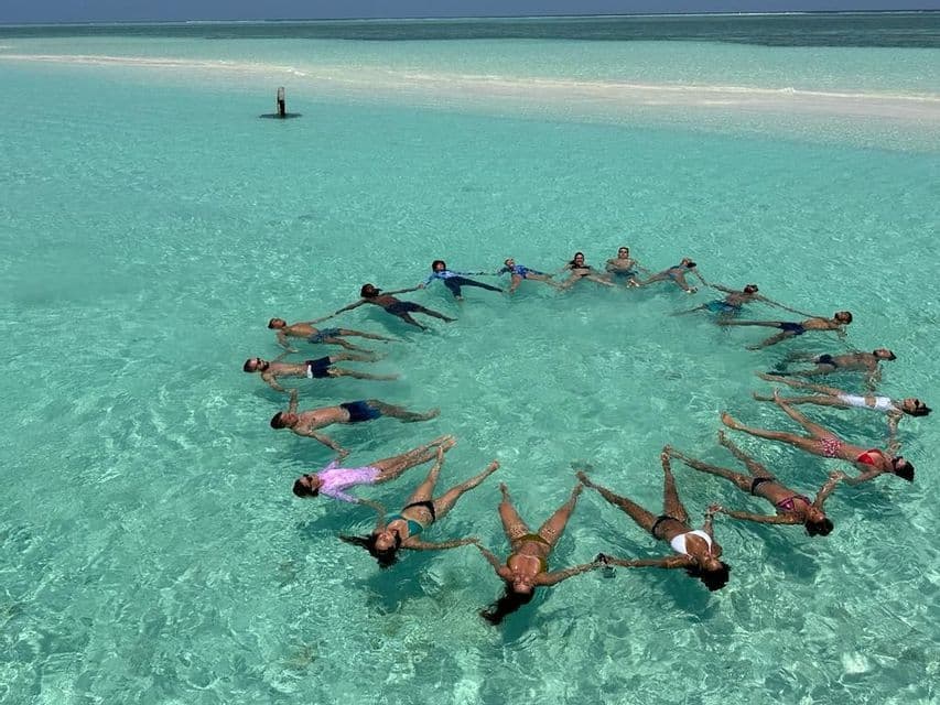 WeRoad Gruppenreise: Menschen halten Händchen und schweben im Kreis auf dem Rücken im klaren türkisfarbenen Wasser.