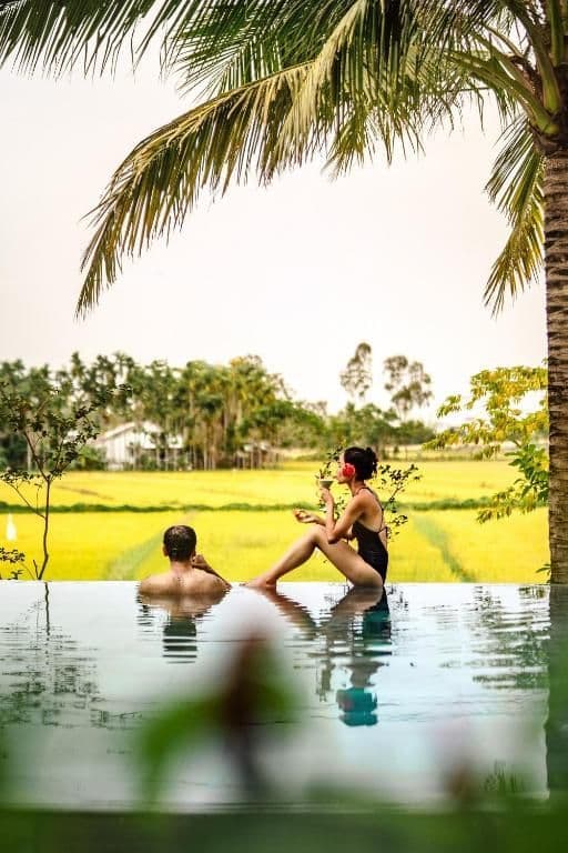 Un hombre y una mujer en un viaje en grupo de WeRoad se relajan en una piscina infinita con vistas a un arrozal amarillo brillante.