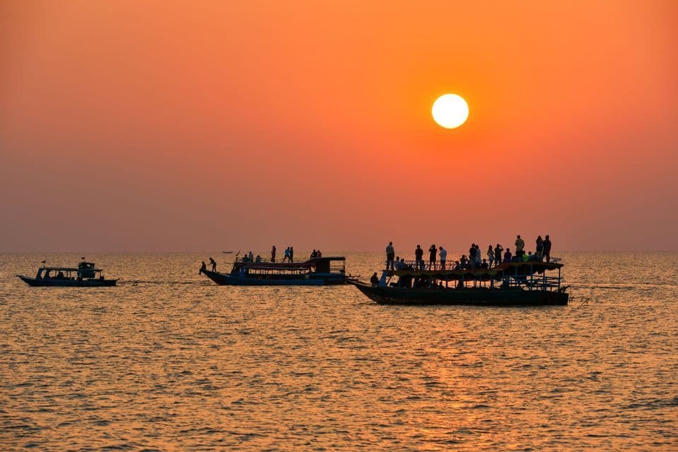 Eine WeRoad-Gruppe ist auf mehreren Booten zu sehen, wie sie den Sonnenuntergang über dem Wasser beobachtet.