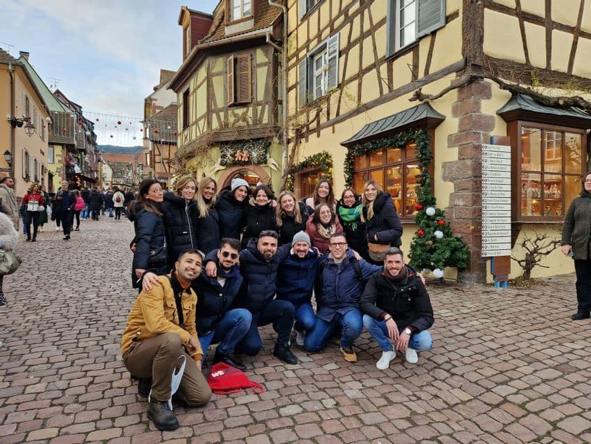 Un gruppo WeRoad in posa su una strada acciottolata con edifici a graticcio e decorazioni natalizie.
