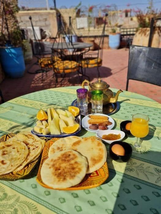 Una colazione tradizionale a base di focaccia, frutta, uova e tè, apparecchiata su un tavolo su una terrazza esterna soleggiata.