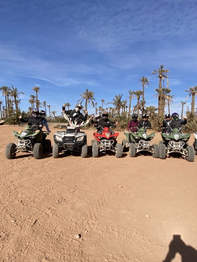 Un gruppo WeRoad in posa con le quad nel deserto con palme.