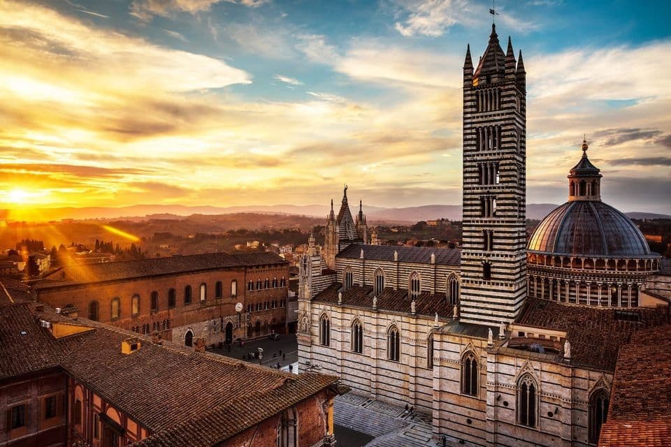Una vista aérea de una catedral con un campanario y cúpula a rayas, dominando una ciudad histórica al atardecer.