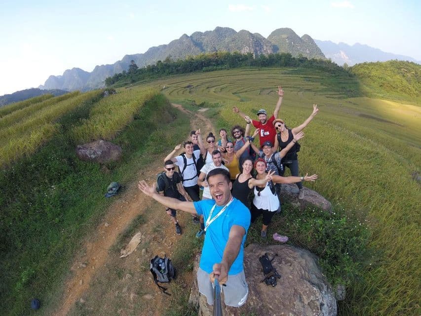 Un viaje en grupo de WeRoad se toma una selfie sonriente en un sendero con vistas a colinas verdes aterrazadas y montañas distantes.