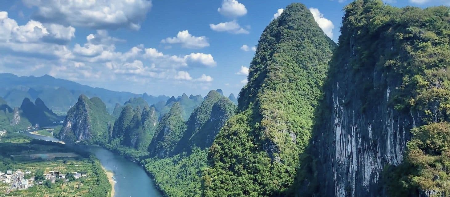 Veduta aerea di un fiume che serpeggia in una valle di lussureggianti montagne carsiche verdi, sotto un cielo azzurro con nuvole bianche.