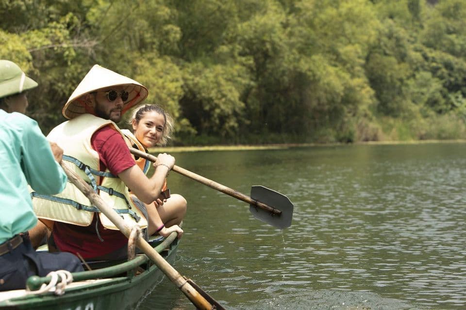 Un viaggio di gruppo WeRoad in barca su un fiume, con un uomo dal cappello conico e una donna che sorride alla macchina fotografica.