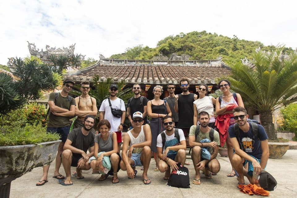 Un groupe WeRoad pose pour une photo devant un bâtiment traditionnel au toit de tuiles, entouré d'une végétation luxuriante.
