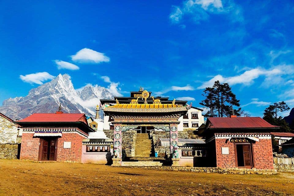 An ornate monastery with a golden-roofed gateway sits in a courtyard below a massive snow-capped mountain.
