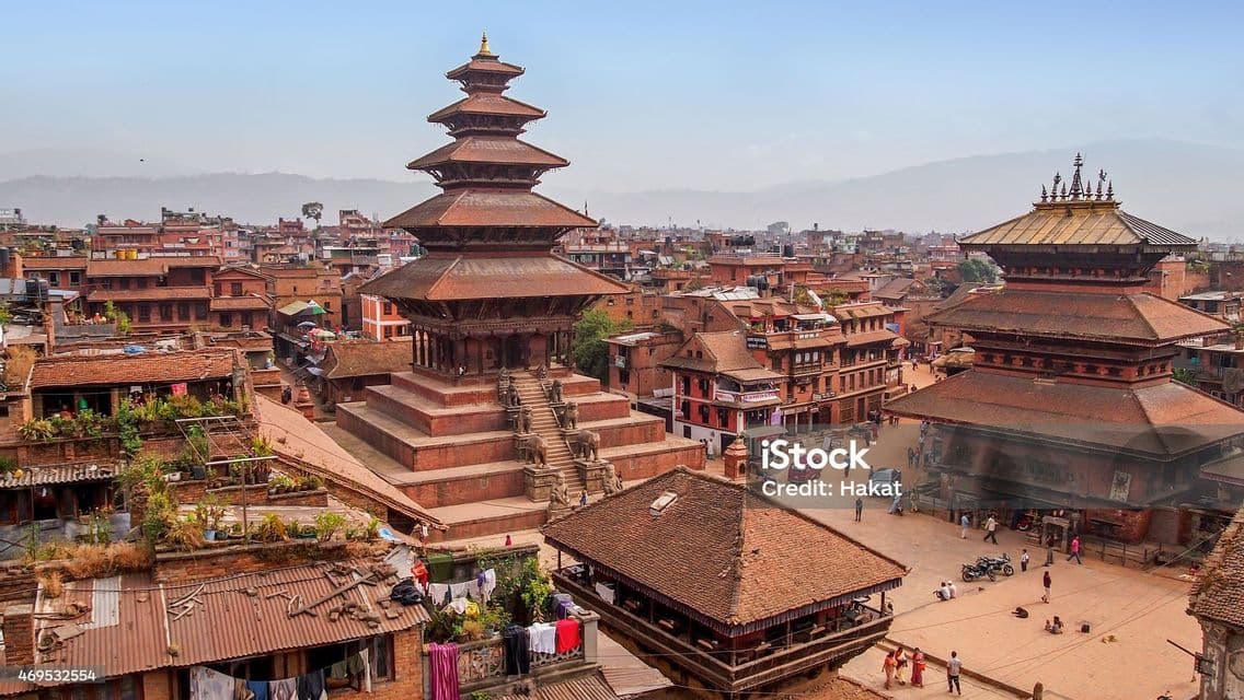 Vue aérienne d'un temple pagode à plusieurs niveaux dans une ville historique avec des bâtiments en briques rouges et des collines lointaines.