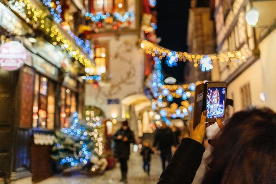 Una persona fotografía una calle urbana iluminada con luces navideñas de colores por la noche.