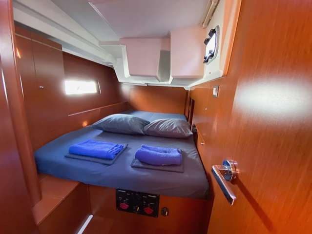 Ein ordentlich gemachtes Doppelbett mit blauer Bettwäsche in einer kompakten Bootskabine mit holzgetäfelten Wänden und einem kleinen Bullauge.