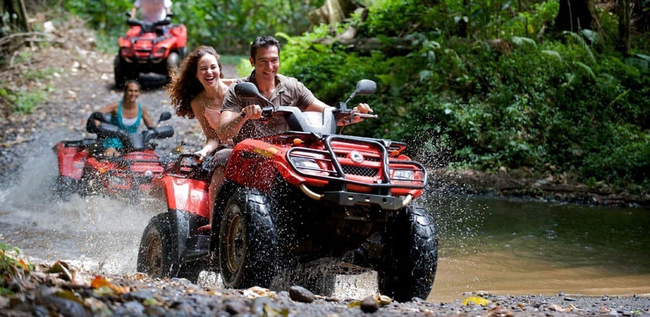 Un groupe WeRoad souriant lors d'une virée en quads rouges dans un ruisseau peu profond d'une jungle luxuriante, éclaboussant l'eau.